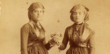 Iglesias - Due giovani donne in abito tradizionale con fiori in mano in interno di studio fotografico 